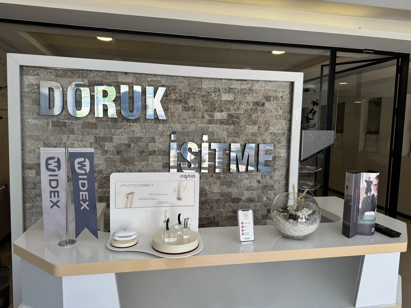 Doruk İşitme Cihazları Ümitköy Şubesi bankosunda Signia cihaz teşhiri ve Widex flamaları